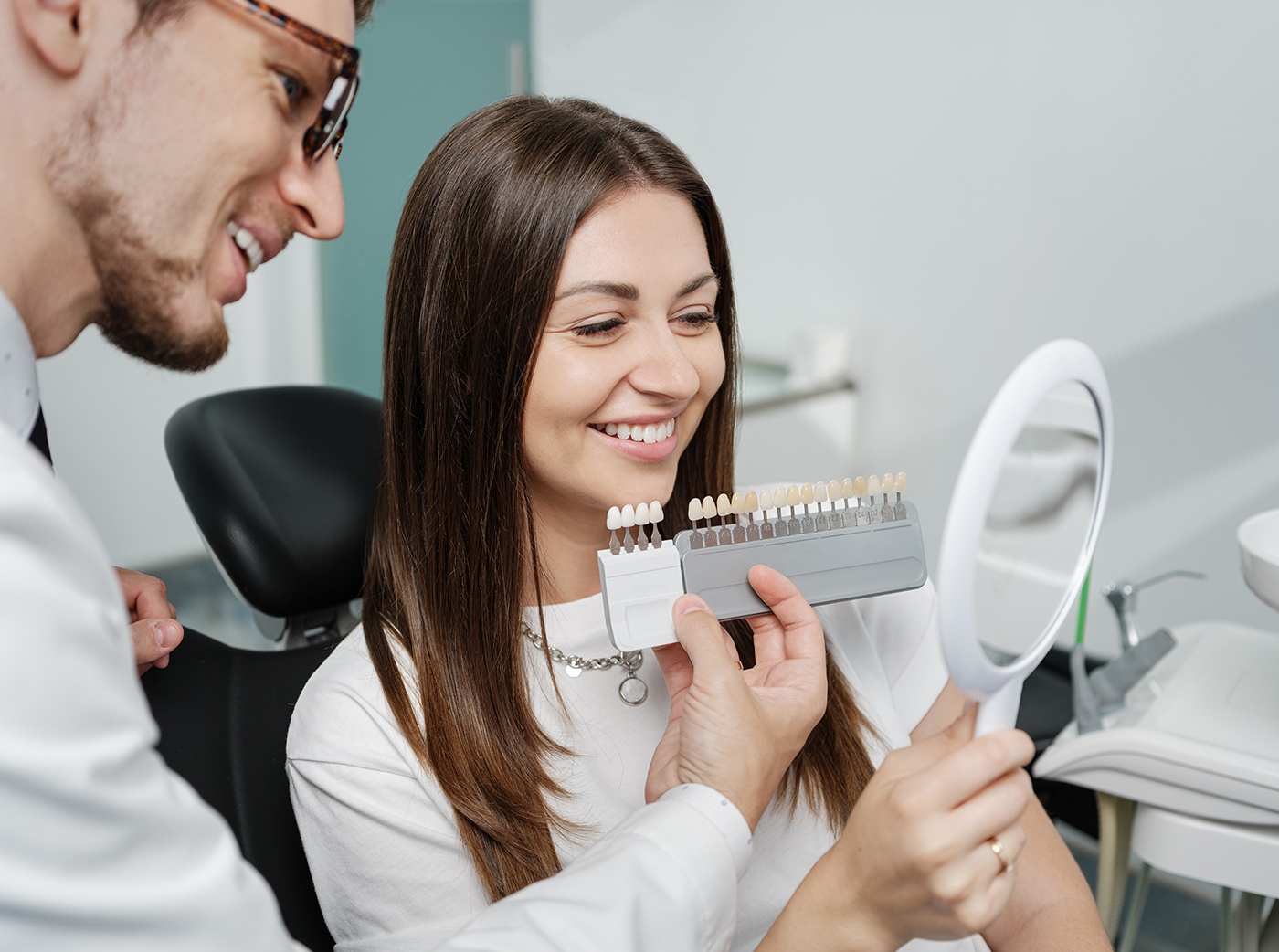 Young man dentist in white coat show veneers enamel color palette for beautiful patient woman