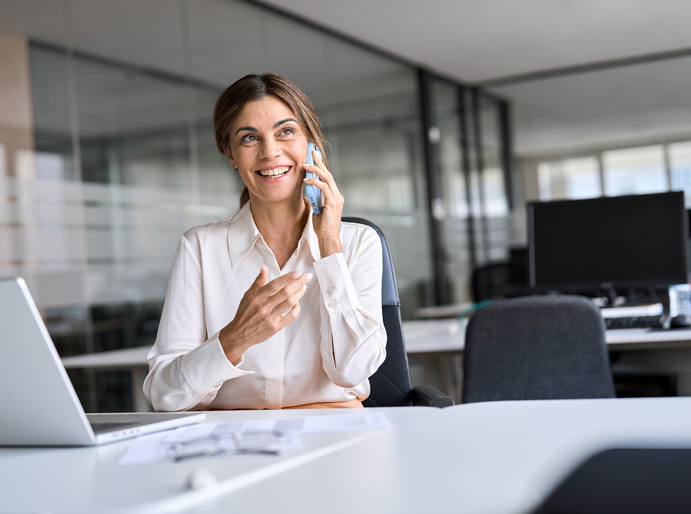 Happy middle aged woman talking on phone making call in office.
