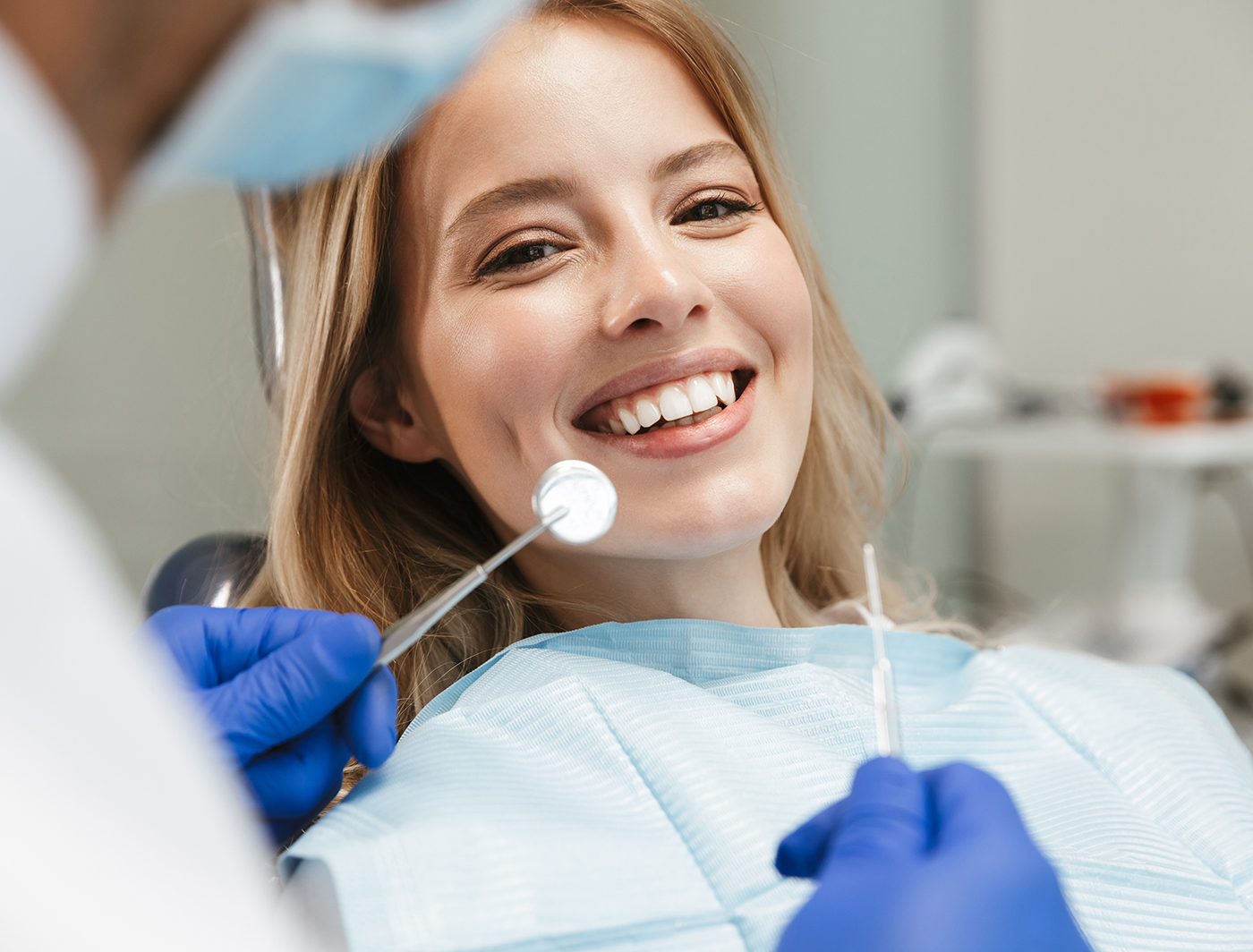 satisfied young woman sitting in dental chair at medical center while professional doctor fixing her teeth